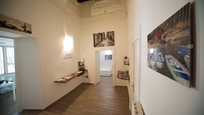A hallway with wooden flooring, white walls, and artwork. There is a desk with chairs and a window on the left. - Home Salvator Rosa 78  (Naples)