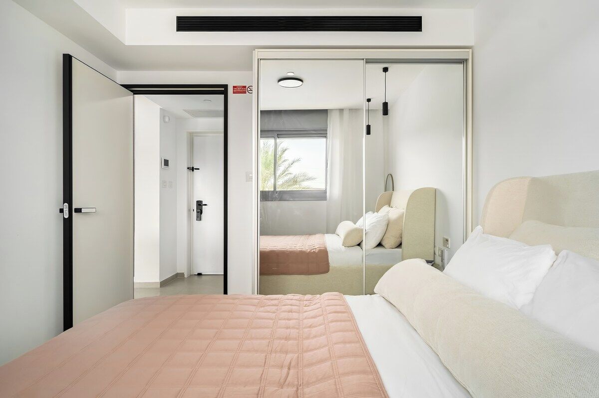 A modern hotel room with a bed, a bedside table, a mirror, and a window.