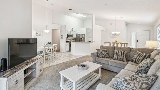 A modern living room with a flat-screen TV, a sofa, a coffee table, and a kitchen in the background. - 4BR Lake Berkley Home, Pool & Game Room (Kissimmee)