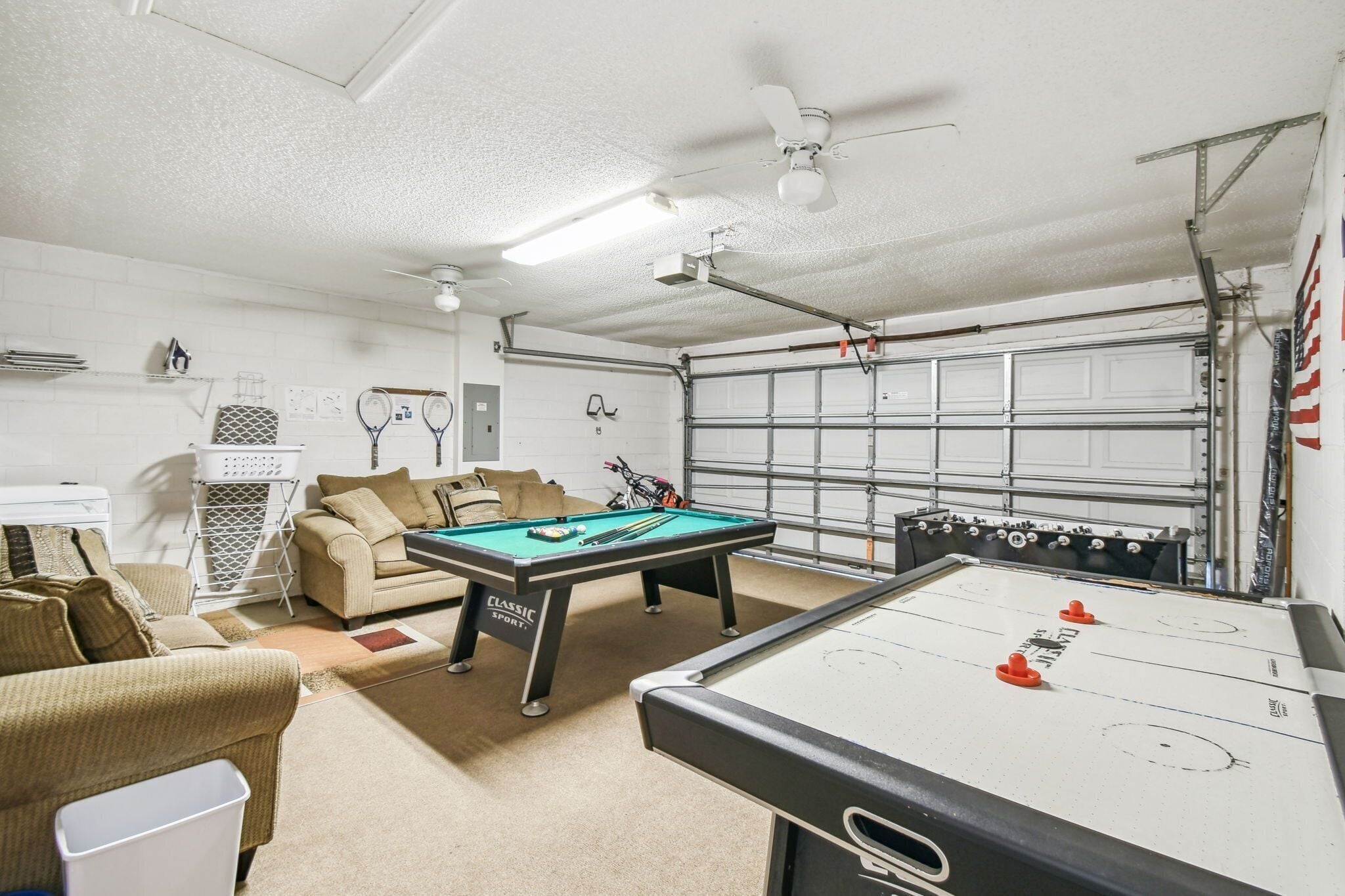 Une pièce équipée d’une table de billard, d’un baby-foot, d’un canapé et d’un ventilateur de plafond.