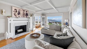 A modern living room with a fireplace, a large sofa, a coffee table, and a view of the outdoors. - The Iconic Anchor Haven at Kennebunk Beach (Kennebunk)