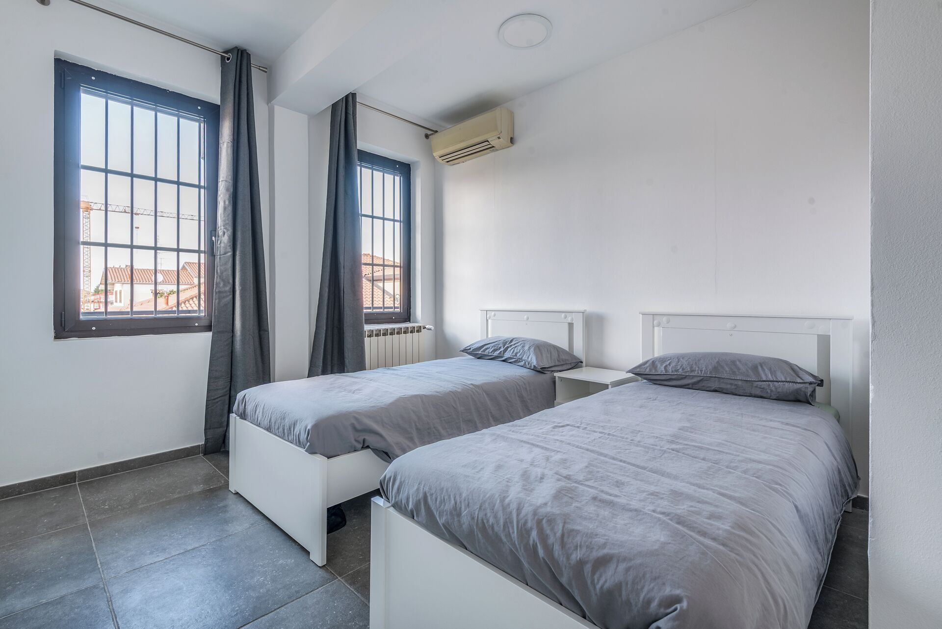 Une chambre avec deux lits simples, une fenêtre avec des rideaux, un climatiseur et un radiateur.