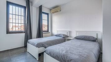Une chambre avec deux lits simples, une fenêtre avec des rideaux, un climatiseur et un radiateur.