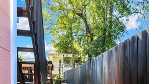 Una escalera de madera que sube a una terraza, rodeada por una valla de madera y un edificio con un muro rosa.