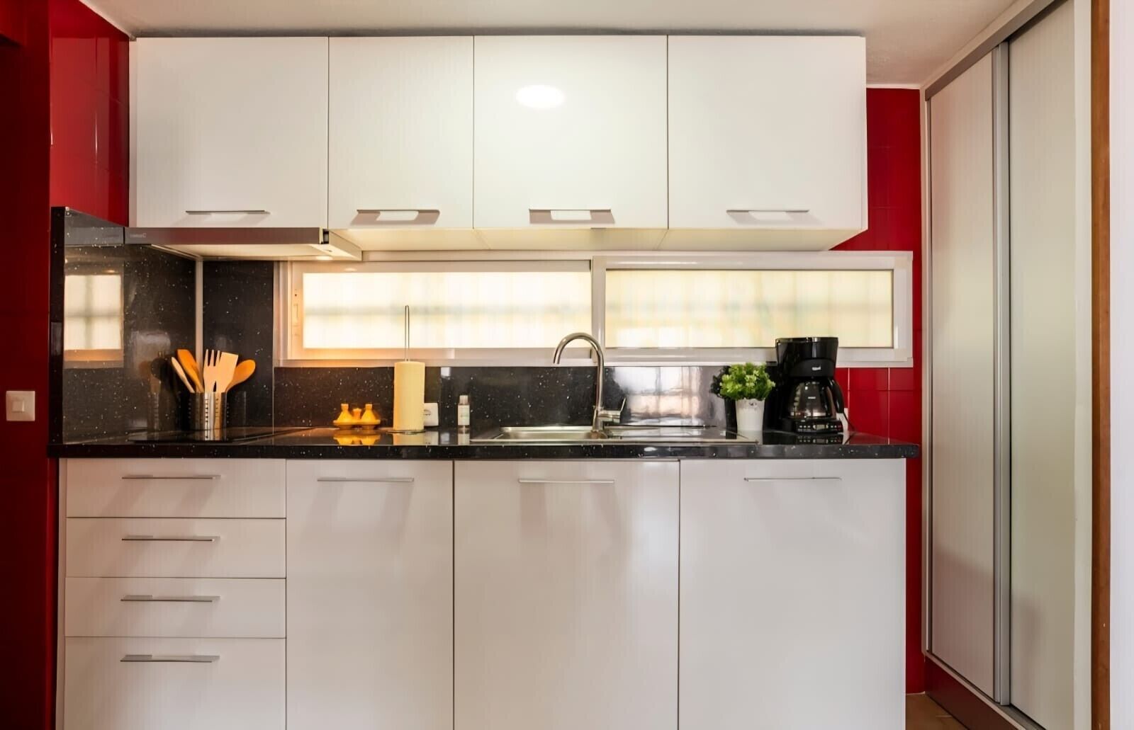Una cocina moderna con armarios blancos, encimera negra, pileta de acero inoxidable y cafetera.