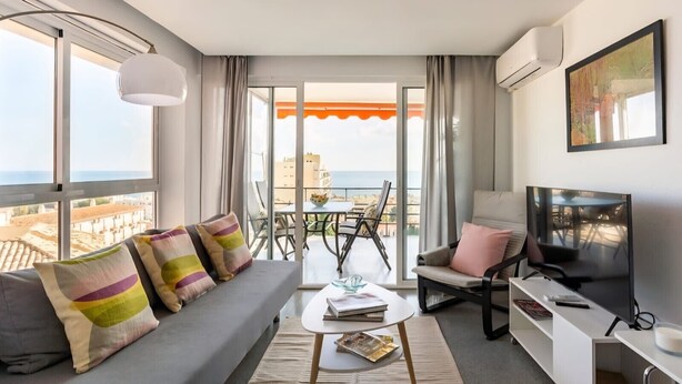 Een moderne woonkamer met een bank, salontafel, televisie en een balkon met tafel en stoelen.