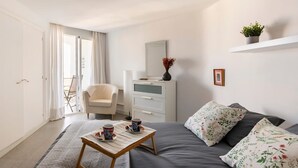 Een slaapkamer met een bed, een stoel, een dressoir, een klein tafeltje met kopjes en een plant op een plank.