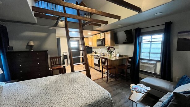 A compact room with a loft bed, a kitchenette, a dining area, and a large window providing natural light. - Extended Loft. Near AT, C&O, Harper`s Ferry (Brunswick)