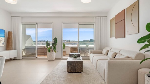 En moderne stue med en sofa, et sofabord og udsigt til stranden gennem store skydedøre.