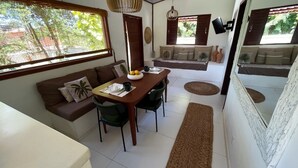 Un coin repas avec une table en bois, des chaises et un canapé. Une fenêtre offre une vue sur la verdure à l’extérieur.