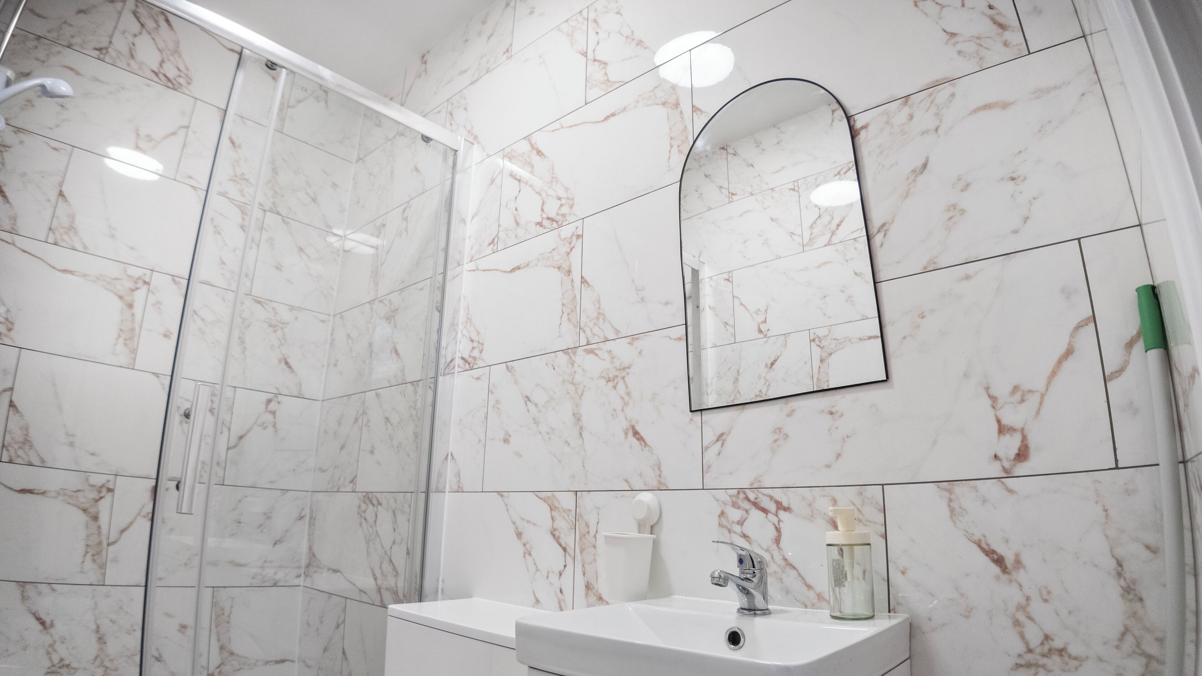 A bathroom with white marble tiles, a sink with a mirror, and a shower area.