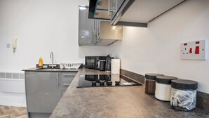 Eine moderne Küche mit einem Edelstahl-Kühlschrank, einer Mikrowelle und einem Gasherd. Auf der Arbeitsfläche stehen zwei Edelstahlbehälter.