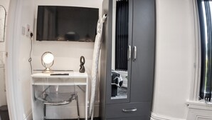 Ein Zimmer mit einem weißen Schreibtisch, einem Spiegel, einer schwarzen Kommode und einem Fenster mit Vorhängen.
