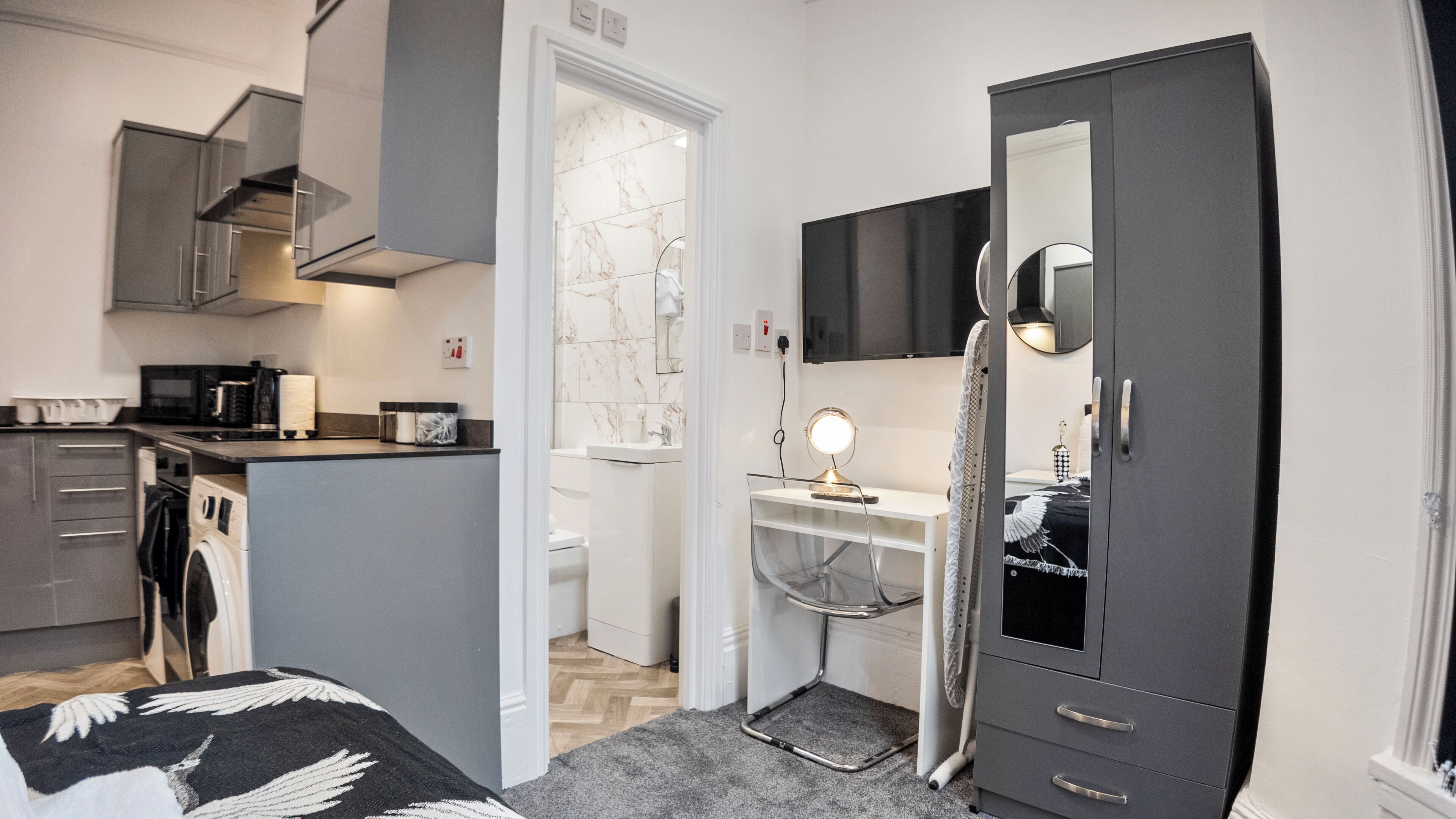 A compact hotel room with a kitchenette, a small bathroom, and a wardrobe.