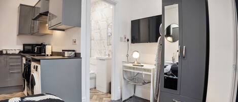 A compact hotel room with a kitchenette, a small bathroom, and a wardrobe.