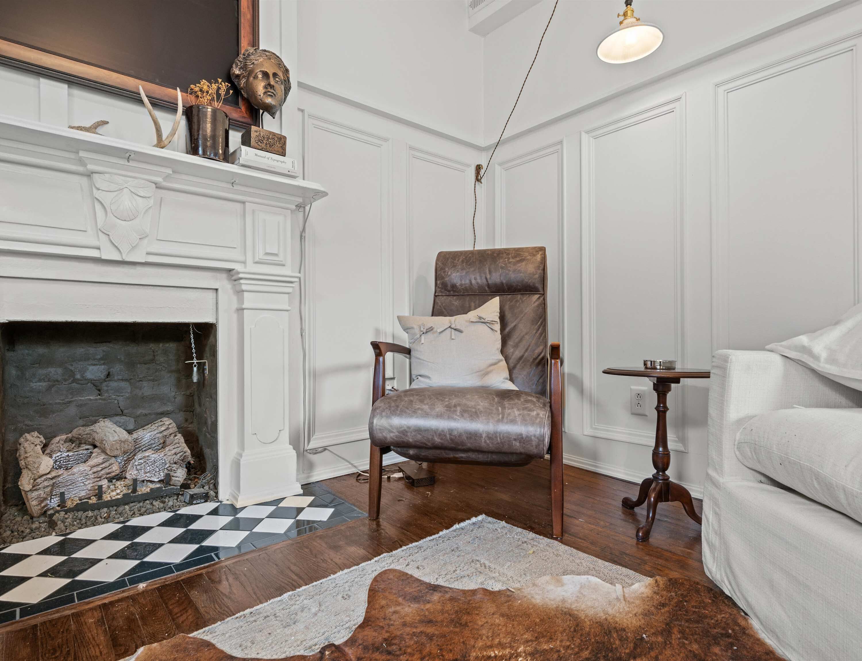 A living room with a fireplace, a leather armchair, a white sofa, a wooden coffee table, and a checkered rug.