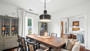 A dining area with a wooden table, black chairs, a hanging pendant light, and a cabinet with glass doors. - The Franklin House, Home for 6 (Franklin)