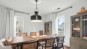 A dining area with a wooden table, wicker chairs, a hanging light fixture, and a cabinet with glass doors. - The Franklin House, Home for 6 (Franklin)