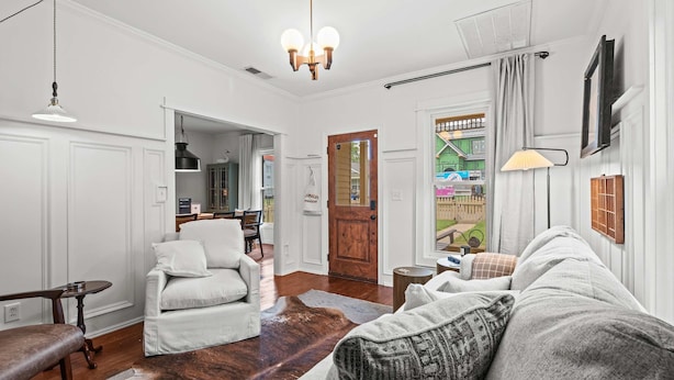 A living room with a sofa, armchair, and a wooden coffee table. There is a chandelier hanging from the ceiling and a door leading to a balcony. - The Franklin House, Home for 6 (Franklin)