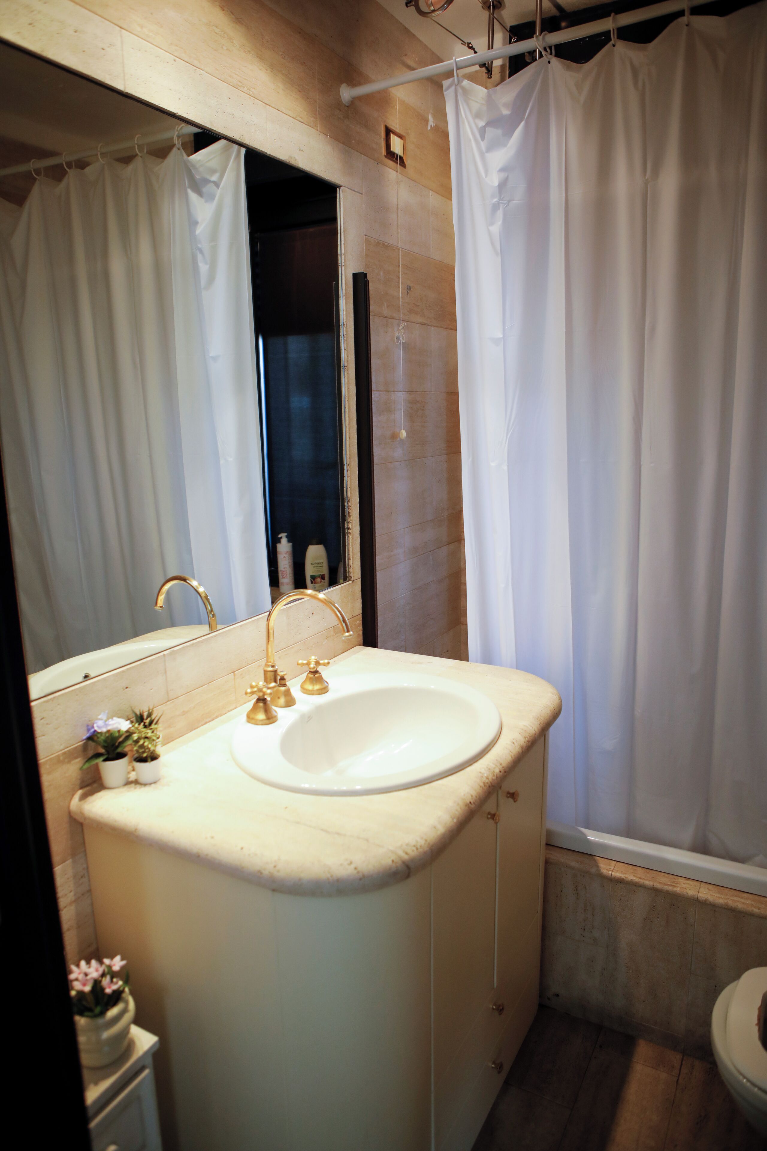 A bathroom with a white sink, gold faucets, a mirror, and a shower curtain.