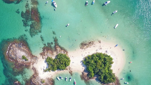 An aerial view of a tropical island with clear turquoise waters, several small boats, and lush green vegetation.