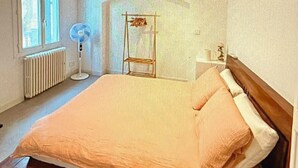 Ein Schlafzimmer mit einem großen Bett, einem Standventilator, einer Heizung und einem Fenster mit Vorhängen.