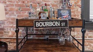 A bar area with a brick wall, a wooden sign reading "BOURBON ST", and various bottles and glasses on shelves. - Modern Soulard • WiFi • Laundry • Queen • Menard (St. Louis)