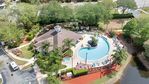 Vista aérea de un complejo turístico con una piscina grande, cancha de tenis y zona de estacionamiento.