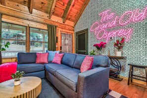 A modern living room with a sectional sofa, a neon sign, patterned wallpaper, and wooden beams. - TheGrandOldOsprey | HotTub+GameRoom 2 min Parkway! (Pigeon Forge)
