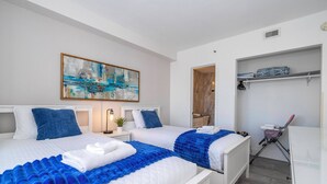 Ein Hotelzimmer mit zwei Betten, einem Gemälde an der Wand, einem Regal mit zusammengelegter Kleidung und einer Kamera auf einem Stativ.