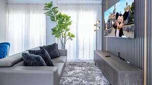 Ein modernes Wohnzimmer mit einem grauen Sofa, einem großen Flachbildfernseher und einer Pflanze.