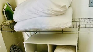 Una stanza piccola con un letto a castello, uno scaffale con asciugamani piegati e un asse da stiro.
