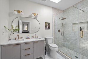 Een moderne badkamer met een marmeren wastafel, een grote spiegel, een toilet en een douche met glazen wanden.