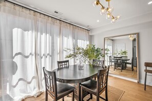 Een eetgedeelte met een ronde tafel, stoelen, een plant en een spiegel die de ruimte weerspiegelt.