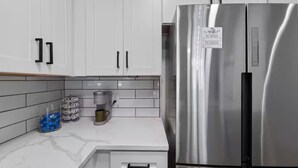 Una cocina moderna con armarios blancos, un refrigerador de acero inoxidable, una cafetera y una jarra para café.