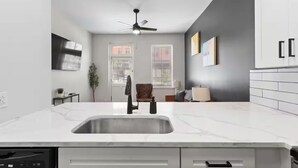 Una cocina moderna con encimera de mármol blanco, lavavajillas integrado y ventilador de techo.