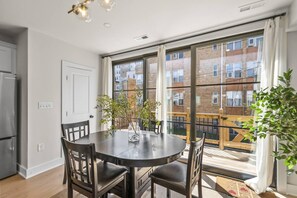 Un apartamento moderno con balcón, un comedor con mesa redonda y una cocina con refrigerador.