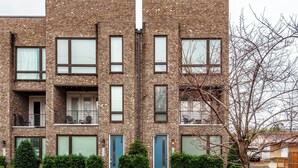 A multi-story brick building with multiple windows and doors, a small tree in the foreground, and a clear sky. - NEW! Townhome End-unit next to Geodis Park! (Nashville)
