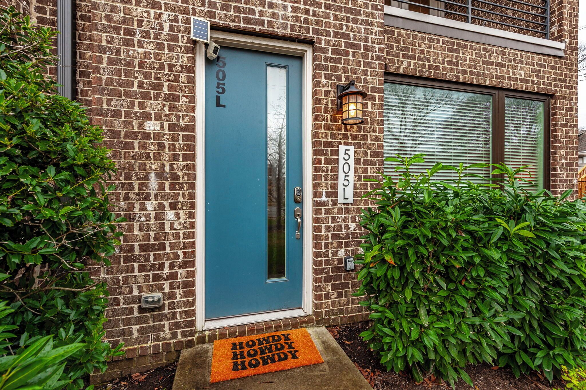 A brick building with a blue door, a number plate, and a doormat.