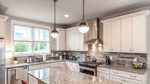 A modern kitchen with granite countertops, white cabinetry, a central island, and pendant lighting. - NEW! Townhome End-unit next to Geodis Park! (Nashville)