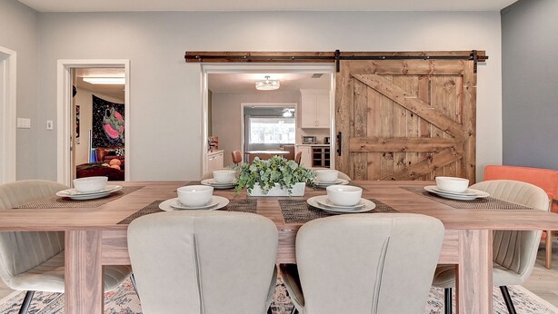 Een eetkamer met een houten tafel voor vier personen, omringd door stoelen, en een schuifdeur in de achtergrond.
