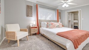 Een slaapkamer met een bed, een stoel, een nachtkastje, een plafondventilator en een kast.