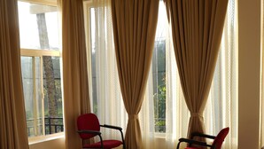 A bedroom with a large bed, two chairs, a ceiling fan, and a window with curtains. - The Thekkady Haritham Residency  (Kumily)