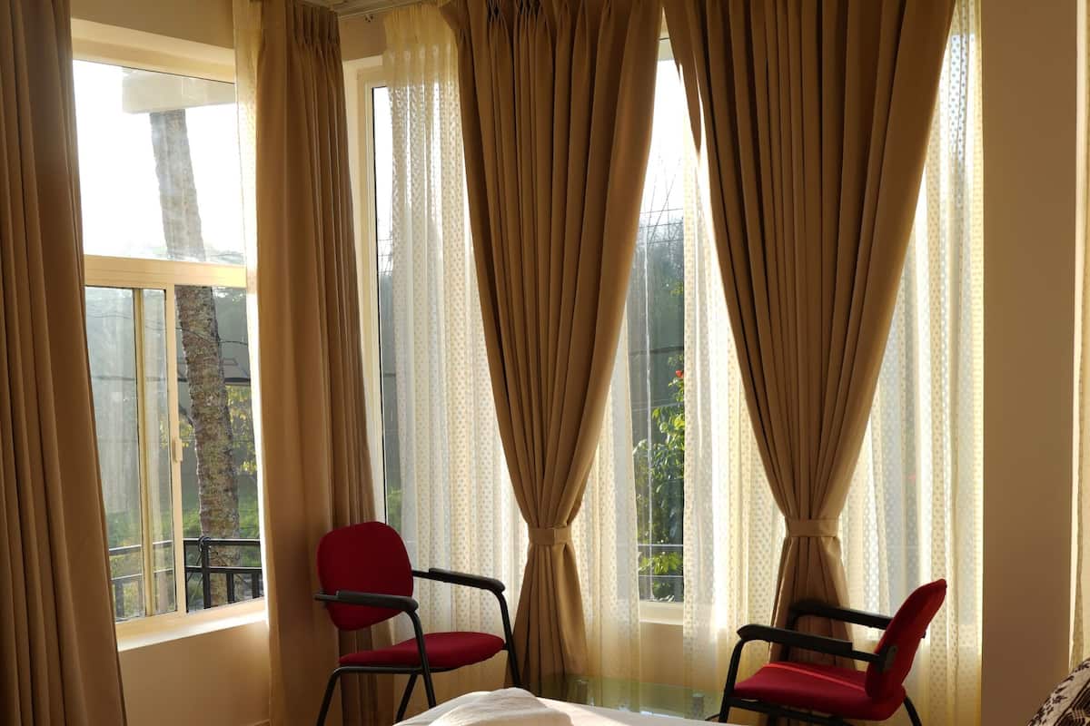 A bedroom with a large bed, two chairs, a ceiling fan, and a window with curtains.