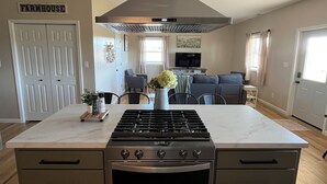 A kitchen with a central island, a stove, oven, and a large range hood.
