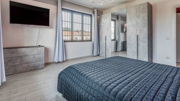 Ein modernes Schlafzimmer mit einem großen Bett, einem flachbildfernseher an der Wand und einem großen Spiegel, der den Raum reflektiert.