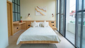 Um quarto moderno com uma cama grande, cabeceira de madeira, um ventilador de teto, uma obra de arte na parede e vista do exterior por grandes janelas.