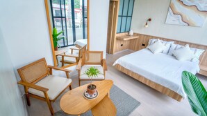 Quarto de hotel moderno com uma cama grande, uma escrivaninha de madeira, duas cadeiras, uma mesinha e um vaso de planta.