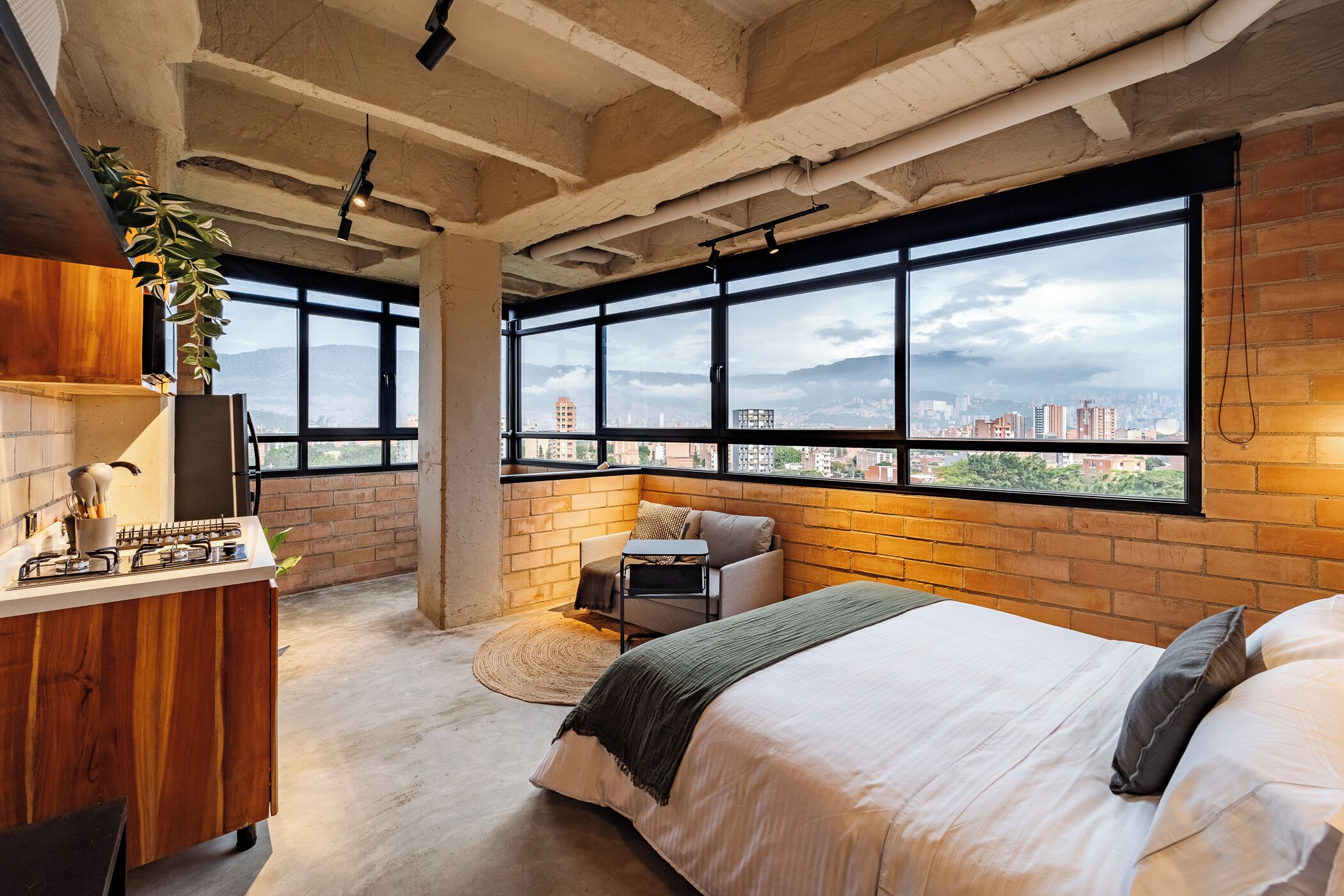 A bedroom with a large window, a bed, a desk, and a plant.