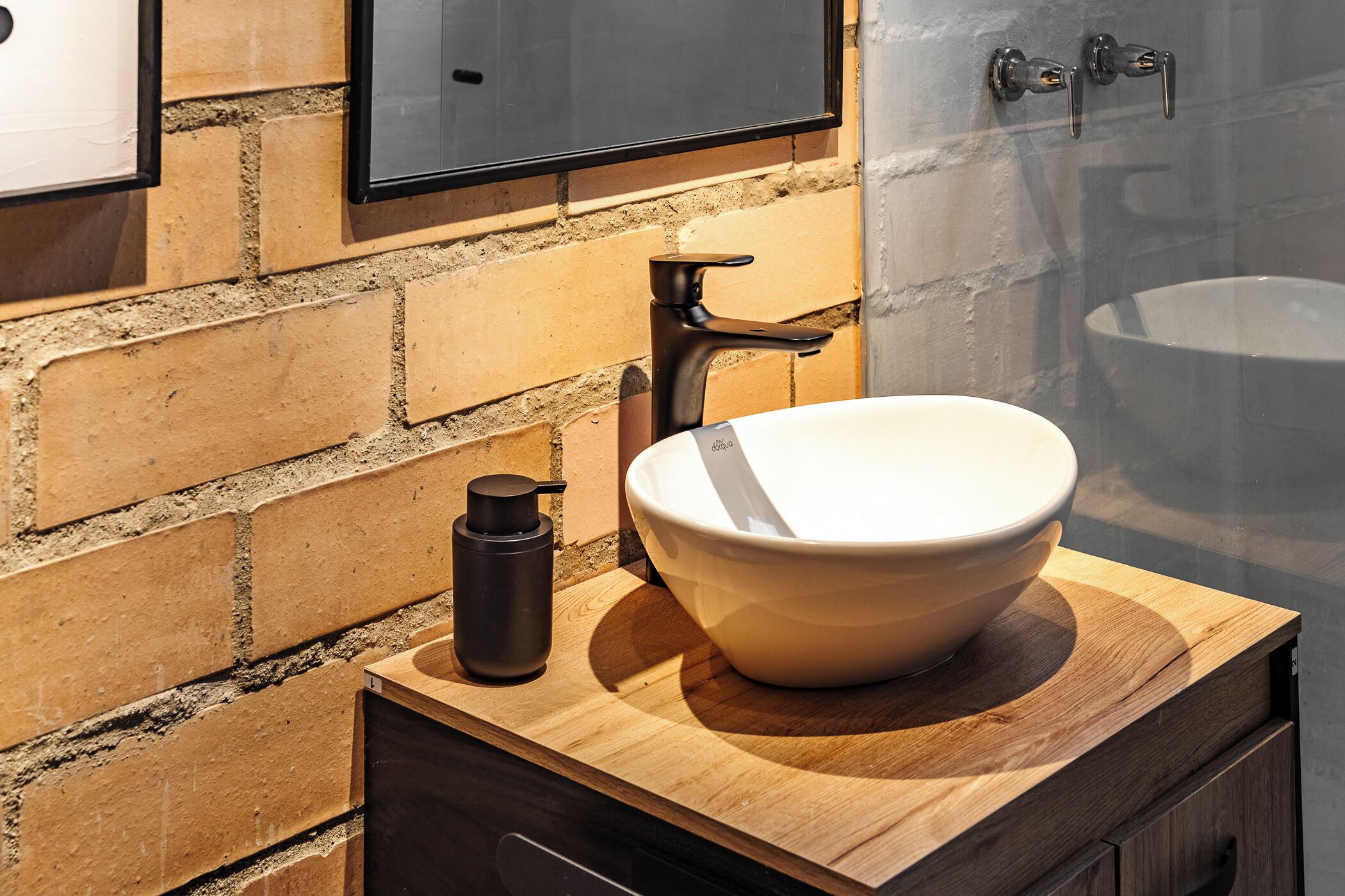A bathroom with a large white sink, a black faucet, and a black bottle on a wooden countertop.